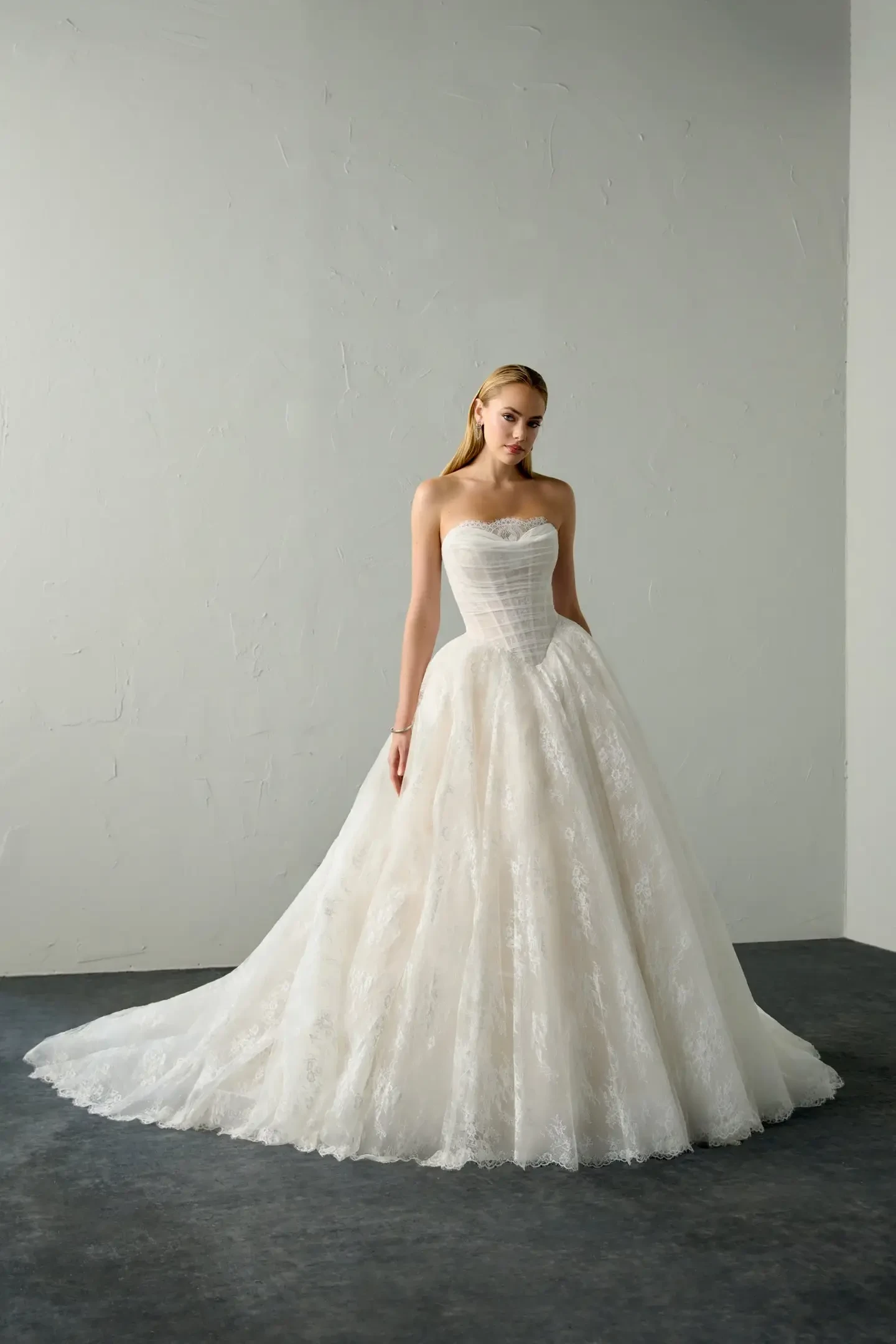 A woman in a white strapless gown with a full skirt stands in a minimalist room.