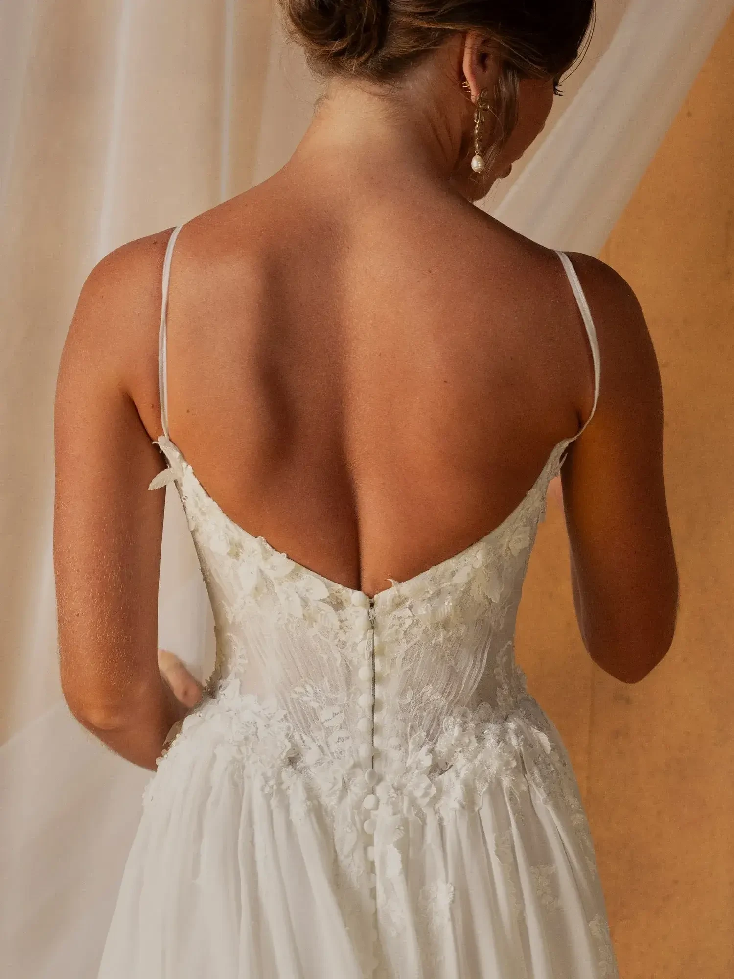 A woman stands with her back to the camera, wearing a white dress with spaghetti straps and floral details on the back.
