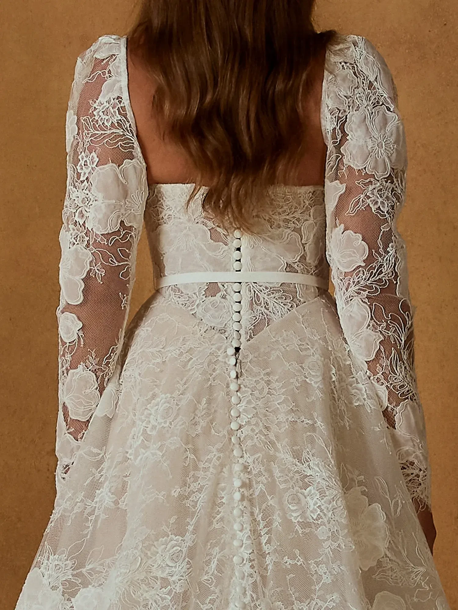 A close-up view of the back of a lace dress with long, sheer sleeves and a button-up detail.